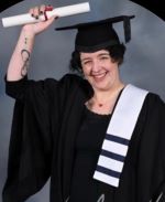 Elaine is wearing a graduation cap and gown and smiling. 