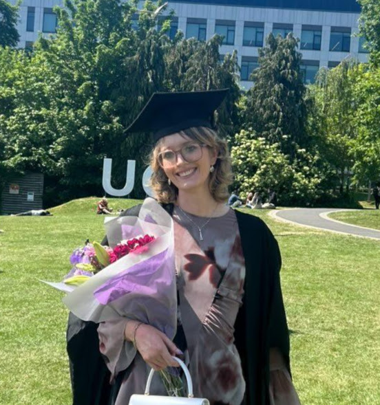 Katie is wearing a graudation cap and holding a bouquet of flowers.